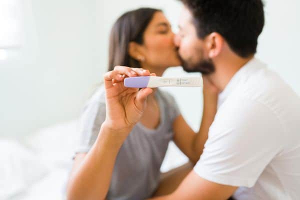 זוג שמתנשק כאשר האישה מחזיקה בדיקת הריון חיובית